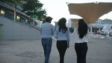 back view of three young business people walking in same direction, talking