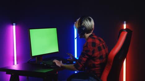 young woman playing on the computer with chroma key screen and celebrating a victory in a room with colorful neon lamps on the wall