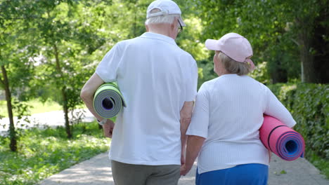 elderly couple walking in park with yoga mats