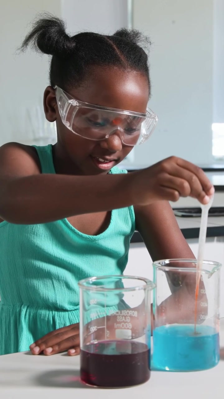 Vertical video: Surveying lab girl in top and goggles using pipette adding orange to blue beaker