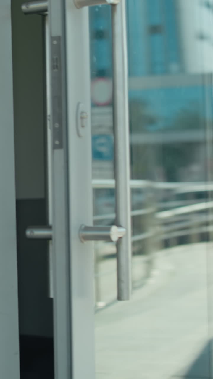 Remote worker walks out of restaurant with reflection of parked cars and urban buildings on glass door, city street in background, focus on movement, and professional casual environment