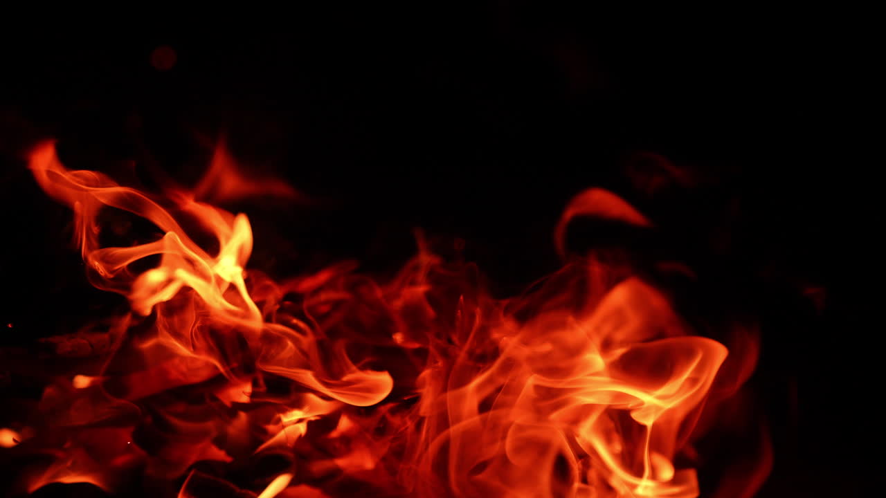 Red flames of campfire are blown by the wind to the ground. Bonfire burn at night. Close up.
