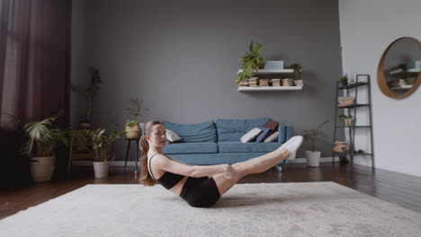 wide shot of an athletic female vlogger giving an online fitness class. she maintains balance with his or her bottom on the ground and keeping the body straight.