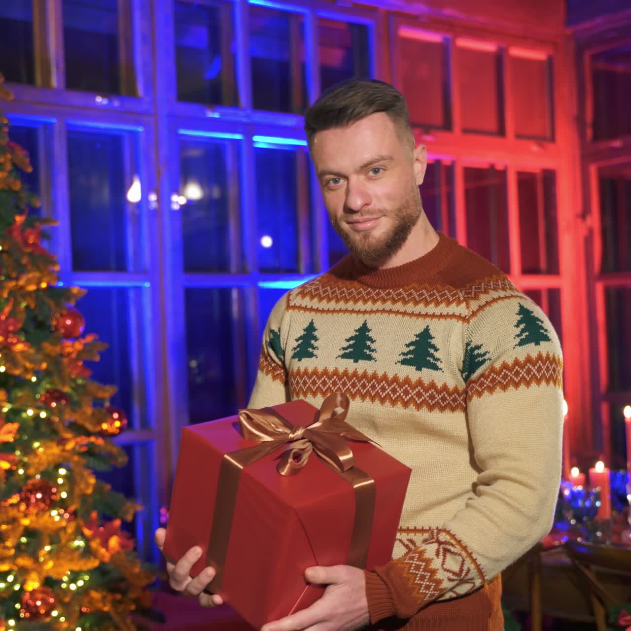 Portrait of cheerful man with Christmas present. Smiling man with gift box standing by Christmas tree and looking on camera.