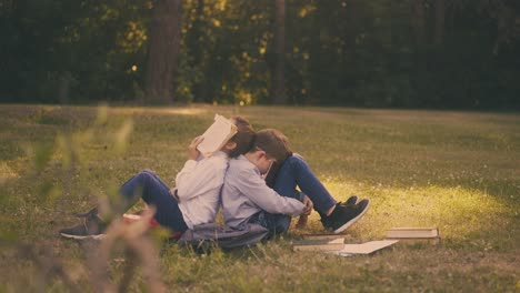 junior schoolboys with textbooks sit on lush lawn in park