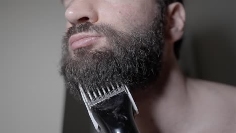 man trimming thick beard with electric razor, close-up