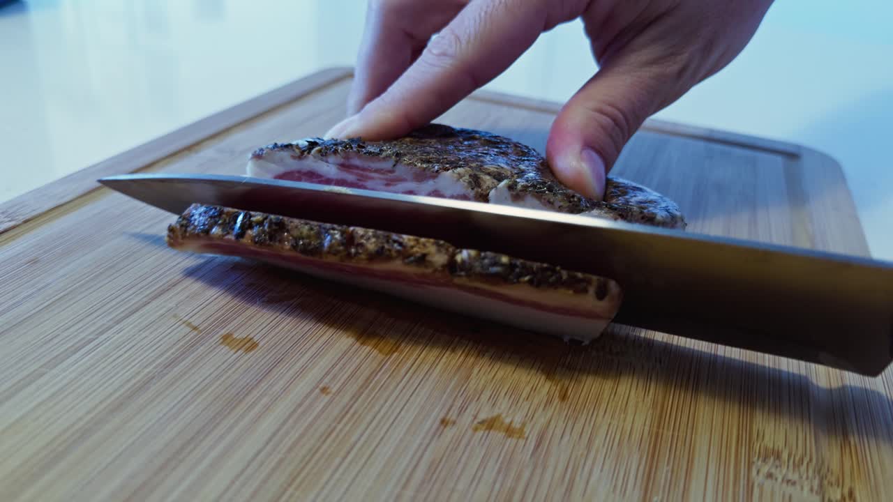 Chef cuts thick slices from a cured guanciale slab on a wood board under natural light