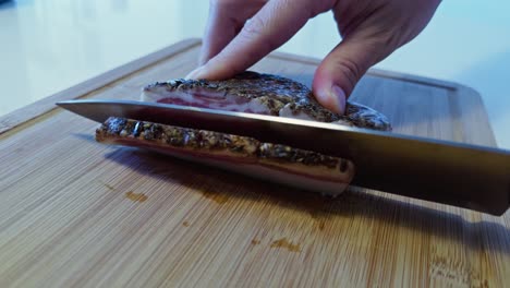 chef cuts thick slices from a cured guanciale slab on a wood board under natural light