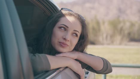 lady leans out of car window and looks at mountain landscape