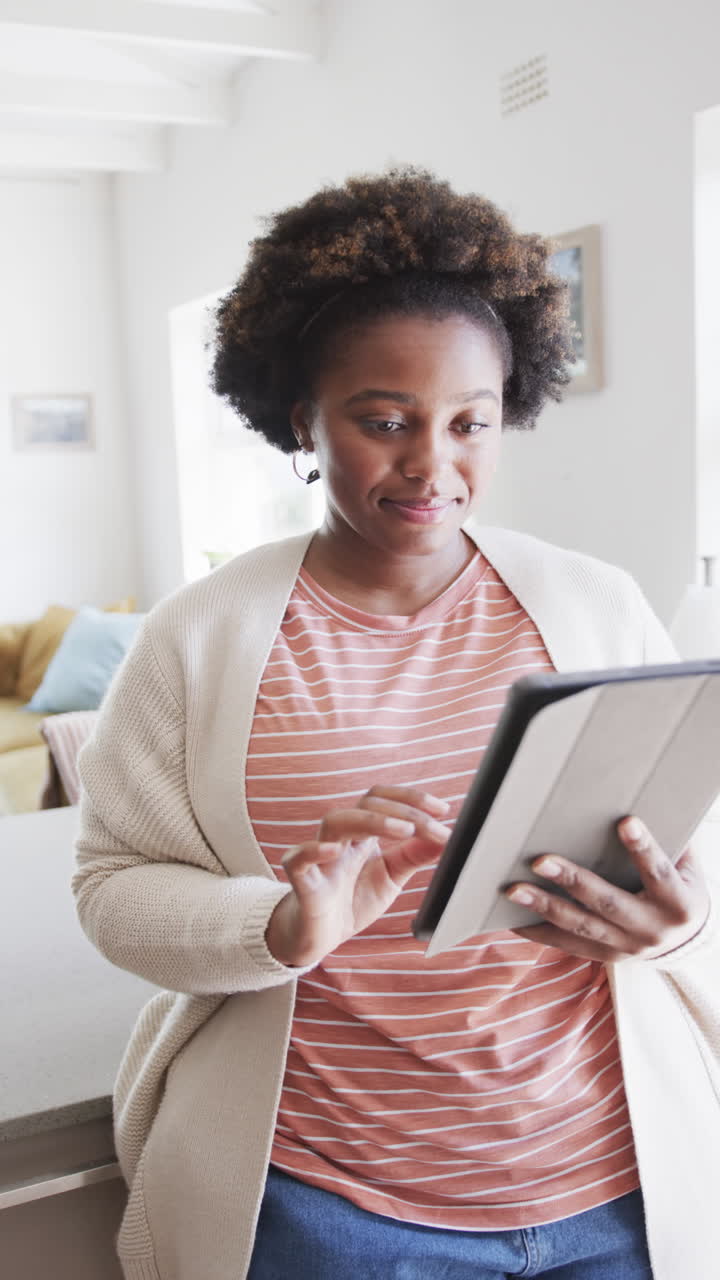 Vertical video of african american woman relaxing and using tablet at home