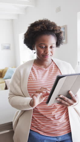 vertical video of african american woman relaxing and using tablet at home