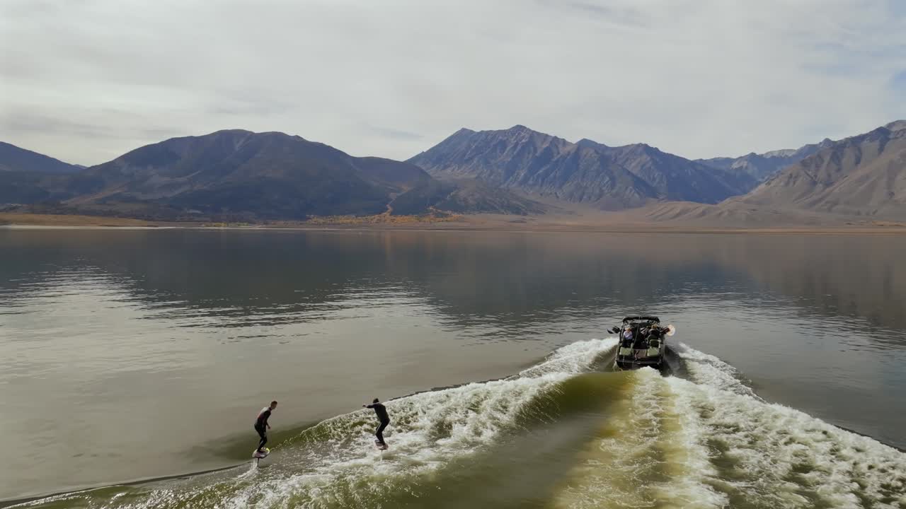 Wake foil surf surfing surfers water sports MB boat left side wave Lake Crowley Mammoth Mountain Lakes California aerial drone golden still calm water morning cloudy autumn follow forward motion