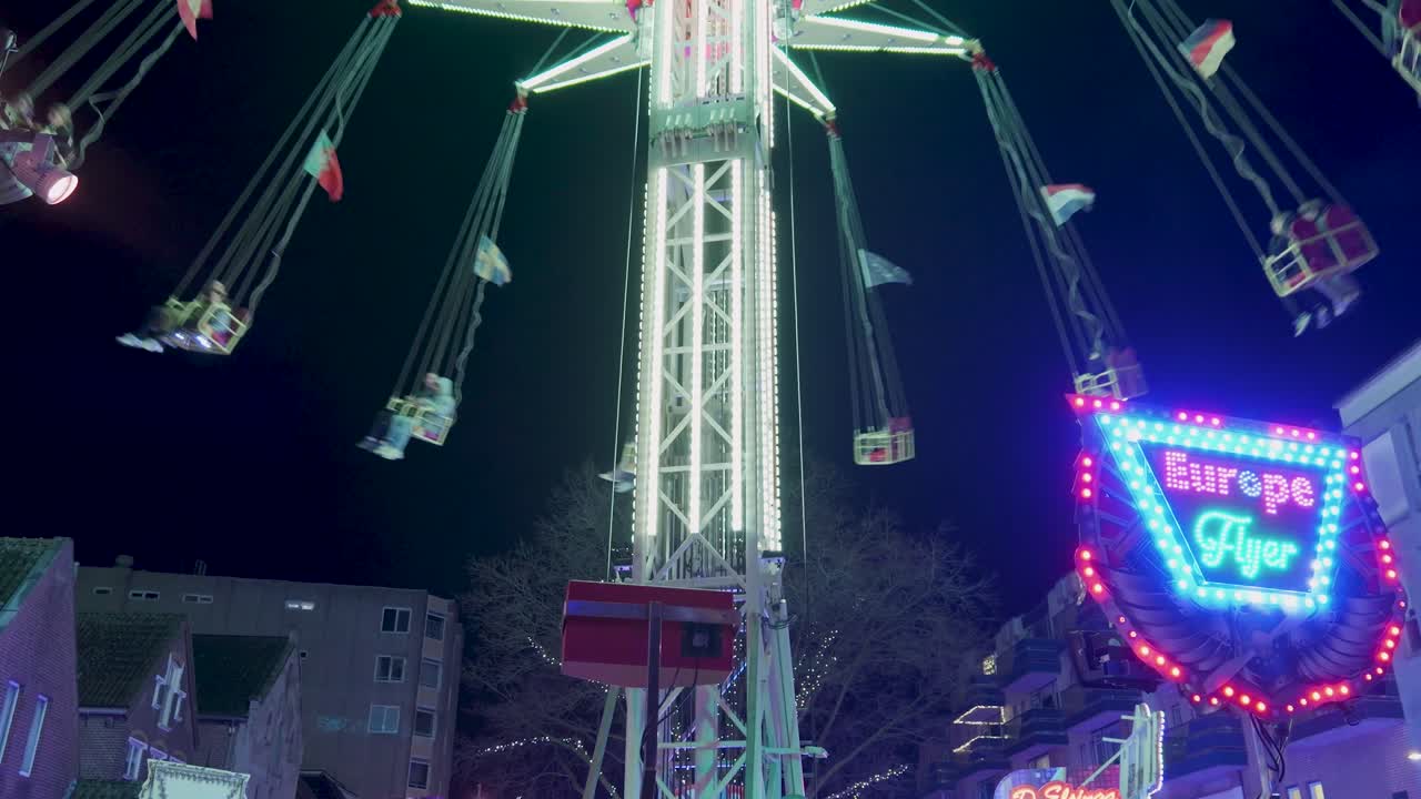 Nighttime at a fair with a Ferris wheel and swing ride