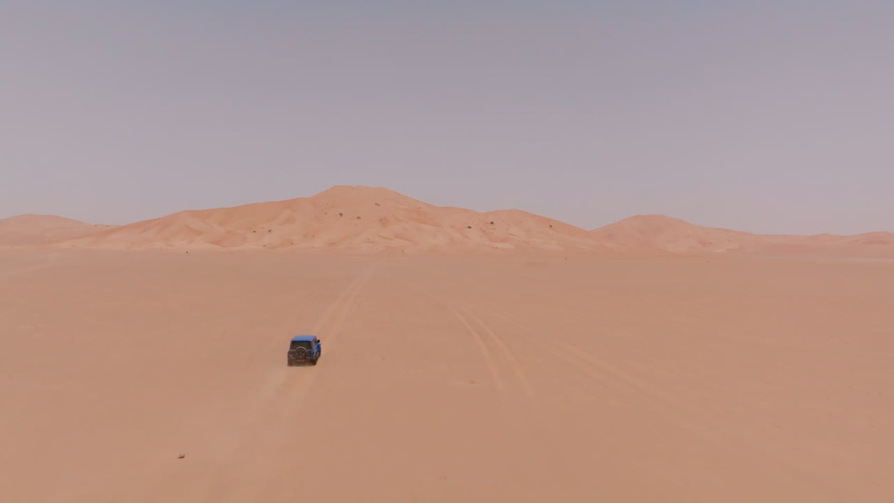 A lone vehicle driving through the vast, barren desert of Oman under the intense summer heat
