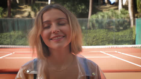 young woman smiling with eyes closed on a tennis court