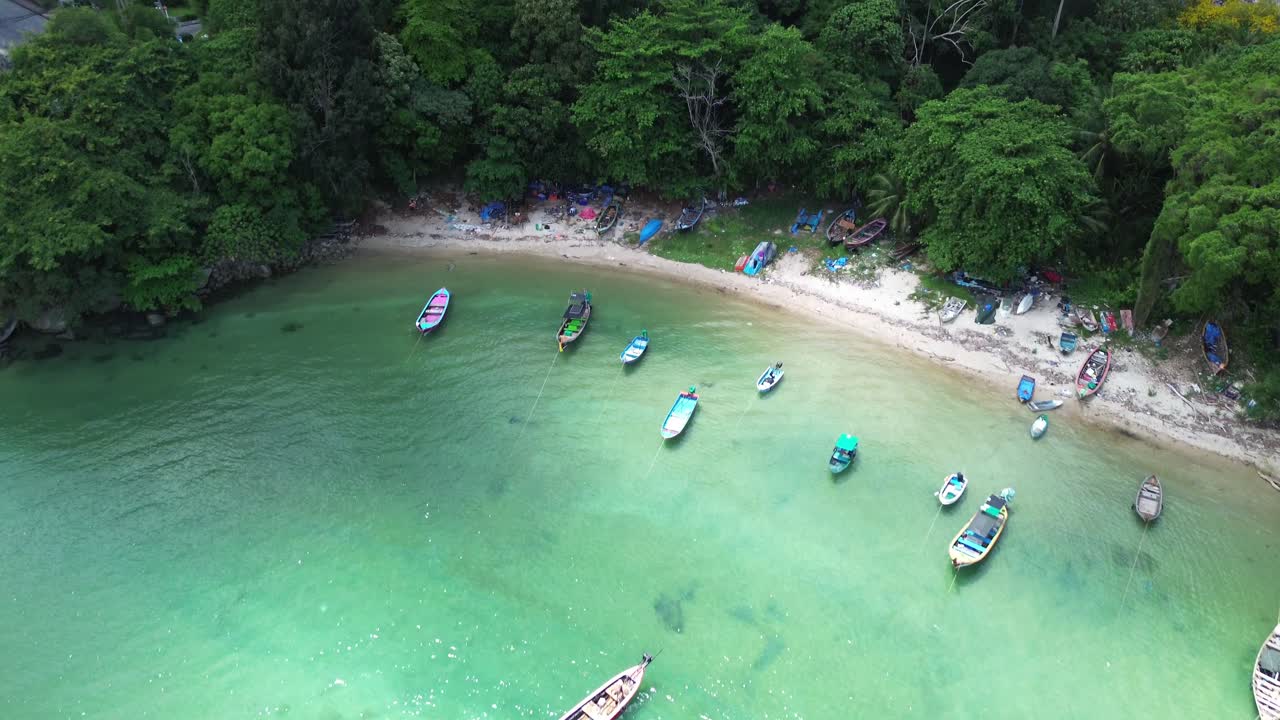 Góc quay drone điện ảnh những chiếc thuyền đuôi dài đậu trên làn nước xanh ngọc tĩnh lặng gần một bãi biển nhiệt đới nhỏ, tạo nên một khung cảnh ven biển yên bình tại điểm đến du lịch Patong, Phuket, Thái Lan.