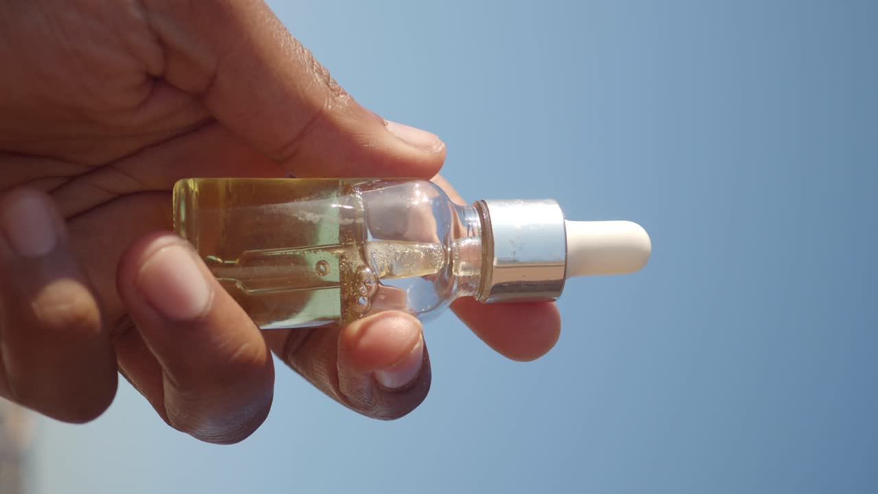 Hand holding a small glass bottle with dropper