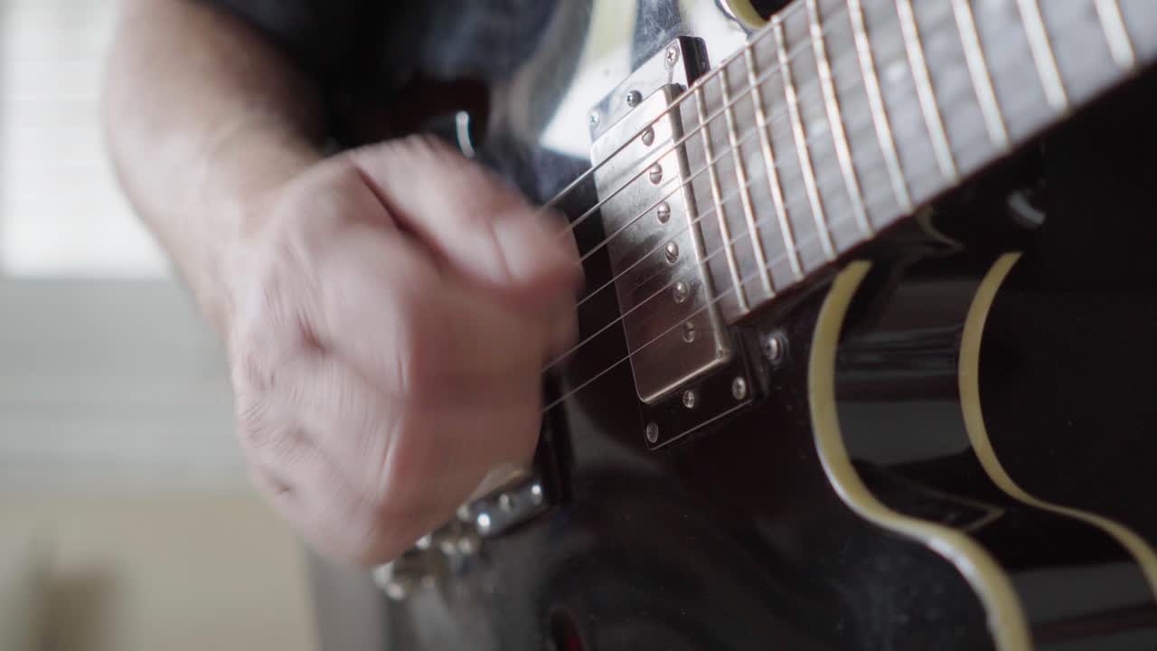 Close-up, side view of a guitarist's right hand playing rhythm on an electric guitar
