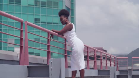 In-a-white-dress,-a-young-black-girl-stands-on-a-rooftop-overlooking-the-cityscape