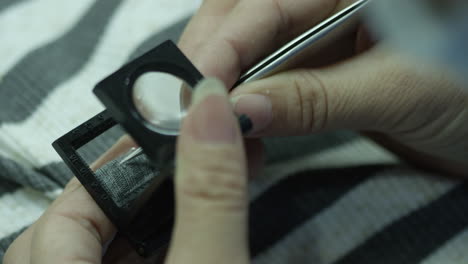 close up on hands of a female factory worker doing a quality check of textile sample with magnifying glass and removing pellets with tweezers, china, asia