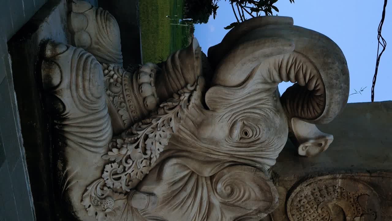 toma vertical de una majestuosa escultura de elefante en bali, situada junto al gong de la paz mundial decorado con banderas nacionales y símbolos religiosos, durante la encantadora hora azul