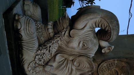 Vertical-Tilt-shot-of-a-majestic-elephant-sculpture-in-Bali,-situated-next-to-the-World-Peace-Gong-decorated-with-national-flags-and-religious-symbols,-during-the-enchanting-blue-hour