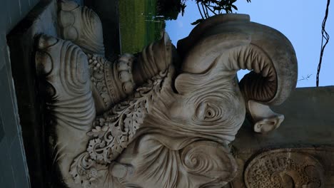 Vertical Tilt shot of a majestic elephant sculpture in Bali, situated next to the World Peace Gong decorated with national flags and religious symbols, during the enchanting blue hour