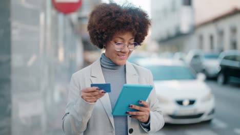 African american woman using touchpad and credit card at street