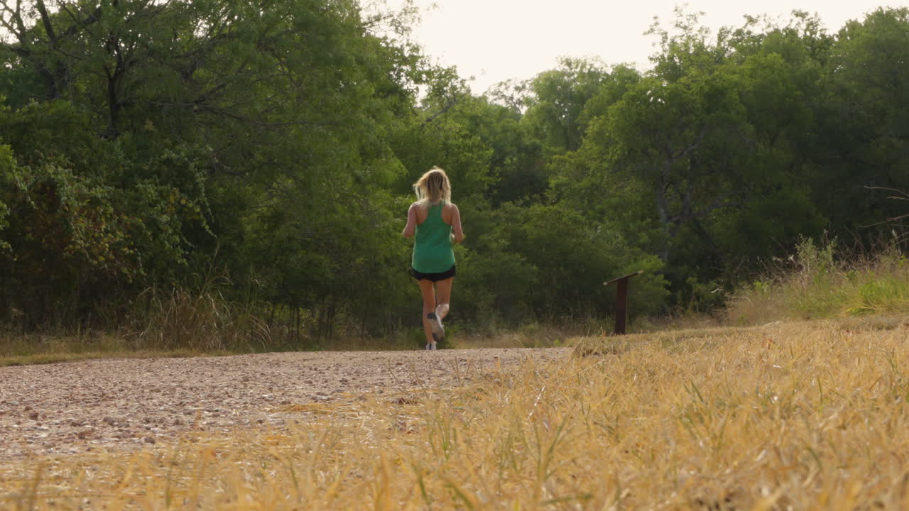 A slow-motion shot captures a woman sprinting on a forest trail, emphasizing her energy and the vibrant greenery surrounding her as she enjoys the thrill of running in nature.