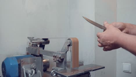 male hand holding knife blade after sharpening on professional grinder lathe