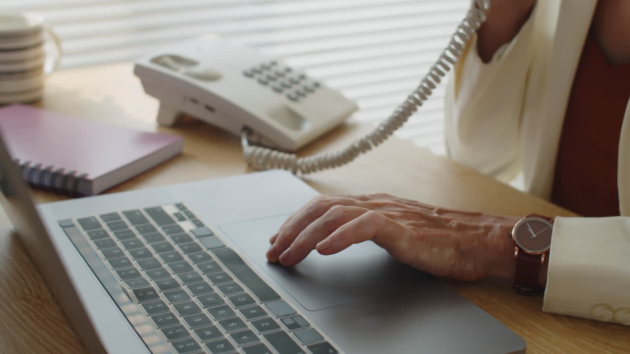 Middle-aged Secretary Agreeing Date of Visit on Phone in front of Laptop