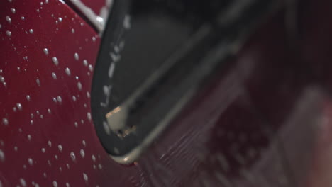 macro view of soap dripping down glossy red car surface during washing process showing texture of water mixed with detergent forming streaks and bubbles on bodywork inside garage environment