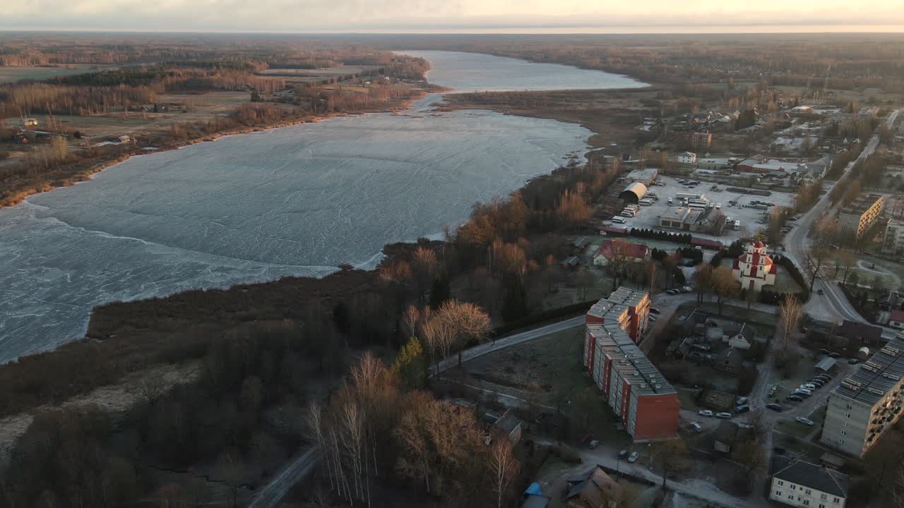 foto aérea de la ciudad de balvi bañada en la cálida luz del atardecer, con edificios urbanos, estacionamientos y un paisaje cubierto de nieve. una escena de invierno pacífica.
