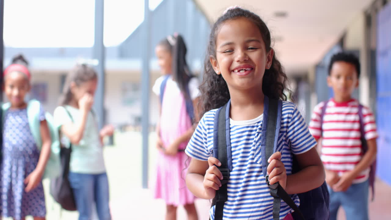 Smiling girl with backpack standing in school hallway with friends in background