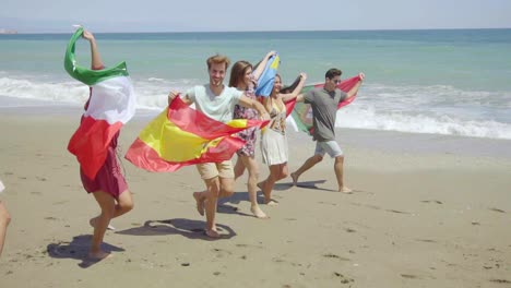 group of friends with flags walking on sunny beach