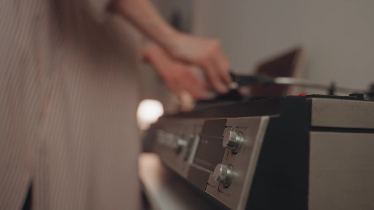 Regolazione attenta dei controlli di un classico giradischi in vinile. Focus sulla sintonizzazione di un vecchio stereo con illuminazione soffusa e vinile. Vista dettagliata delle manopole di un ricevitore stereo vintage che vengono regolate con precisione con un bagliore caldo della lampada.