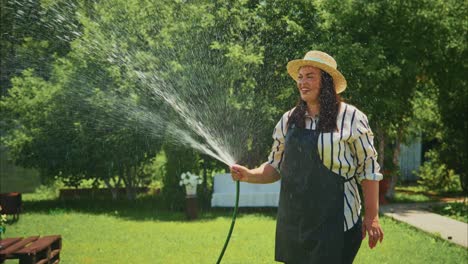 woman watering garden plants with hose in sunny outdoor setting surrounded by greenery