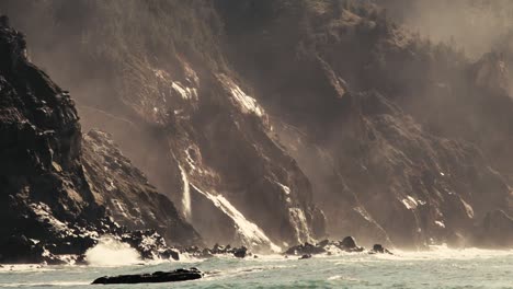 small waves hitting a massive cliff wall with a mystical waterfall on the face