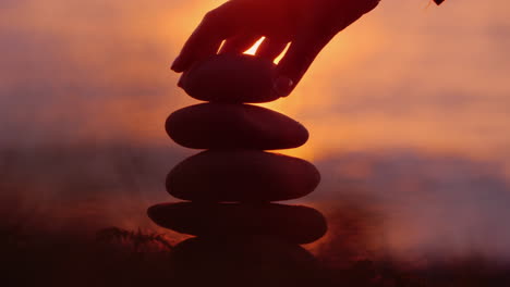 focus on building a tower of stones against the background of the sea where the sun sets