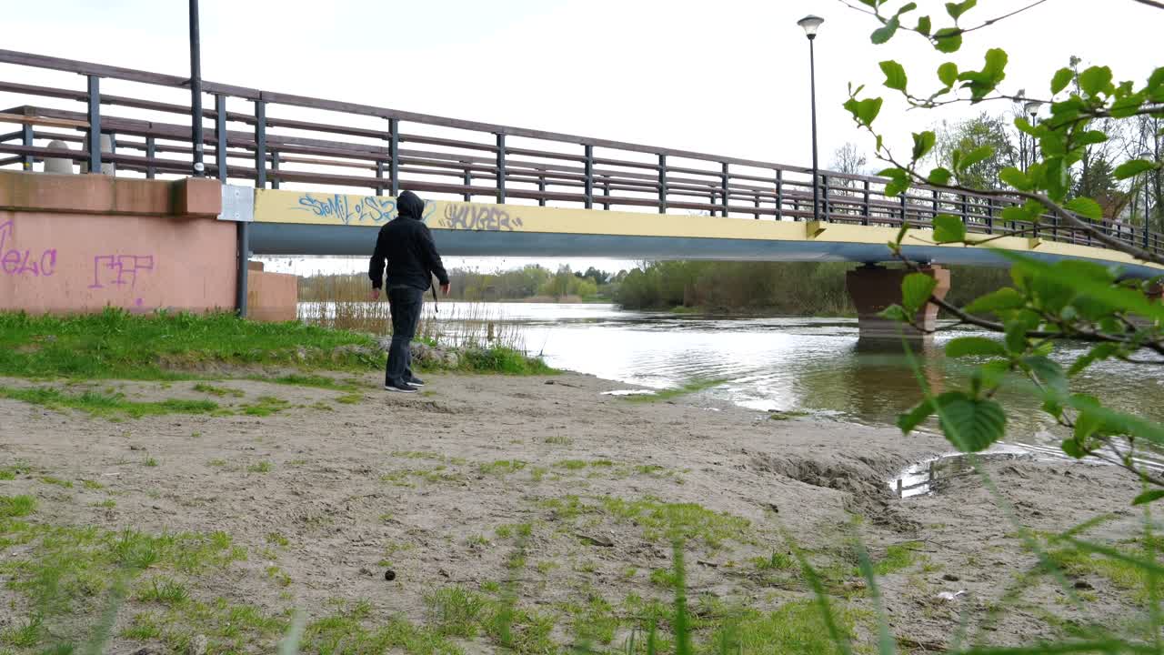 мужчина у берега озера бросает камни в воду