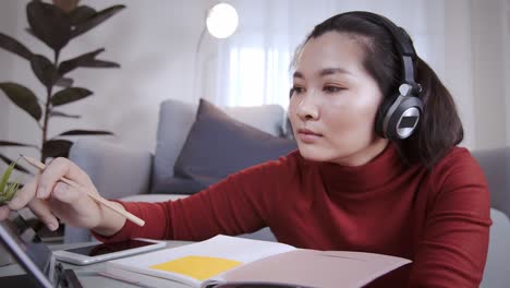Mujer-Asiática-En-Camisa-Roja-Usando-Una-Tableta-Con-Auriculares-Para-Reunirse-En-Línea-En-Casa