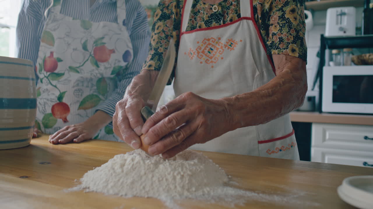 Elderly Woman Cracking Egg into Flour as Cooking with Family in Kitchen
