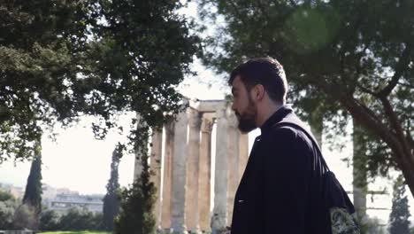 bearded man strolls past ancient greek historical monument the temple of olympian zeus on sunny day with backpack