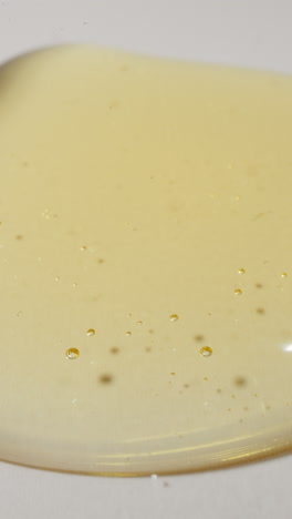 Drops of fresh jojoba oil falling down spreading on white plain surface. Transparent golden liquid with small bubbles. Skincare product macro