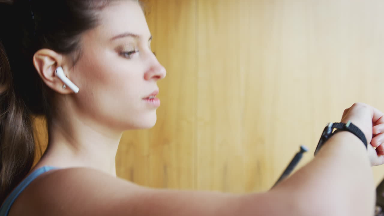 mujer haciendo ejercicio en la cinta de correr en casa usando auriculares inalámbricos comprobando reloj inteligente