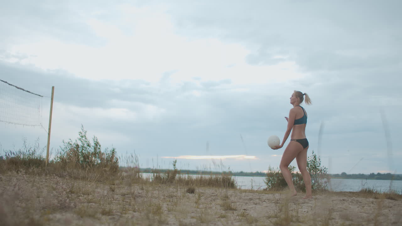 una mujer joven deportiva está sirviendo la pelota en la cancha de voleibol en la playa entrenamiento deportivo de verano y entrenamiento de atleta femenina