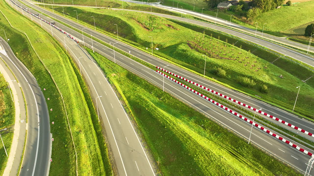 Sweeping aerial shot of the S6 expressway lanes and service roads, curving through lush green, undulating hills and embankments outside Gdynia