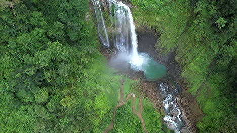 descenso aéreo sobre la cascada eco chontales que fluye hacia un estanque rocoso turquesa rodeado de selva tropical, costa rica