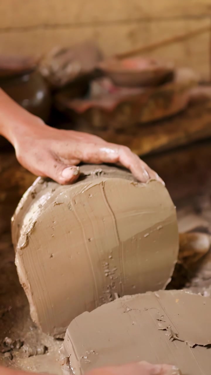 Primo piano delle mani di un artigiano che usano uno strumento a filo per tagliare un blocco di argilla in un tradizionale laboratorio di ceramica.