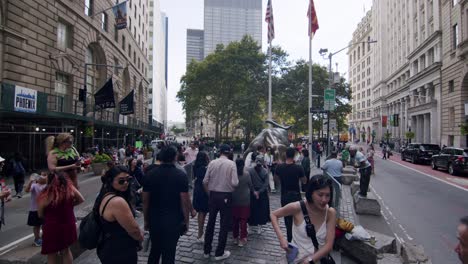 tourists gather near the famous charging bull statue in downtown new york city on a summer day